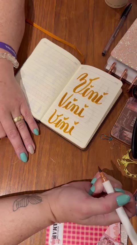 Mão praticando lettering em um caderno durante a oficina presencial.