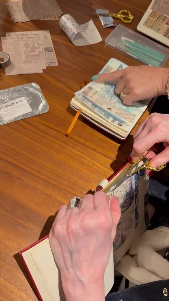 Registro real da oficina presencial: mãos recortando e montando páginas de um travel journal sobre a mesa.