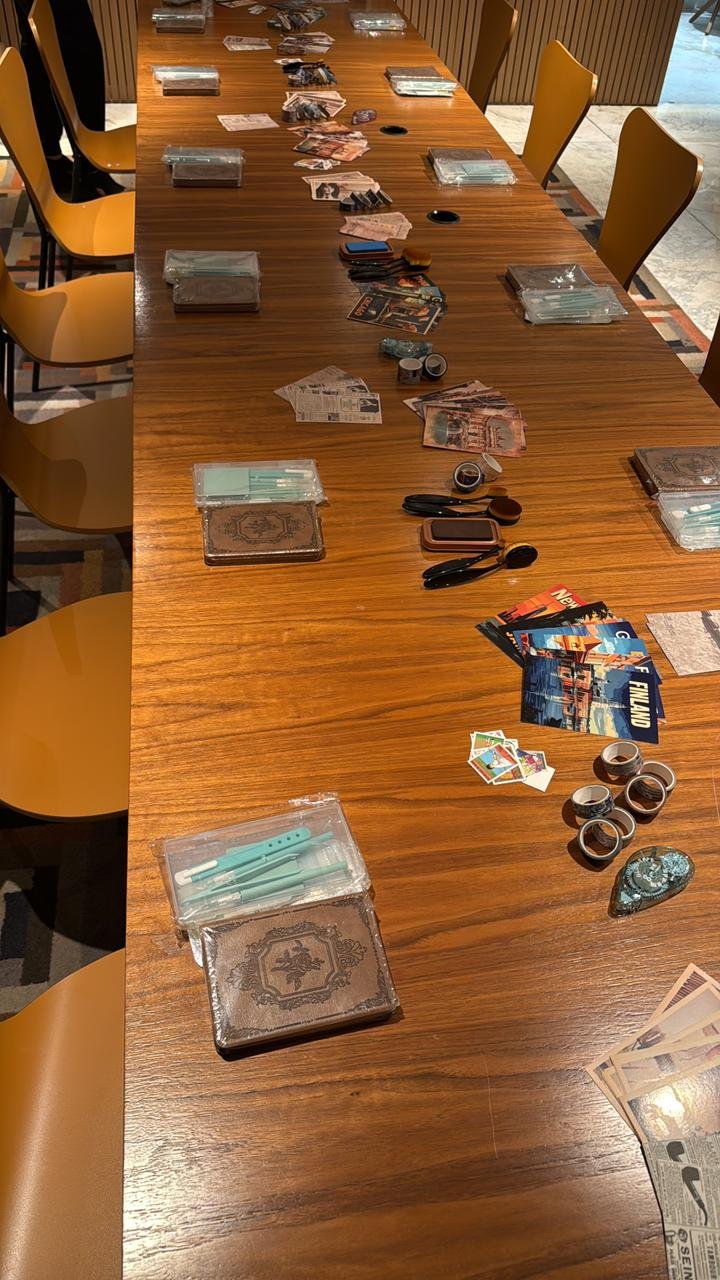 Mesa da oficina presencial da Coração de Papel preparada com cadernos, papéis, recortes e ferramentas.